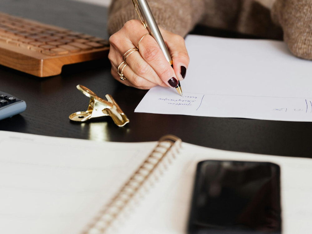 Wedding professional writing notes at a desk with a pen, planner, and phone planning a website refresh strategy.