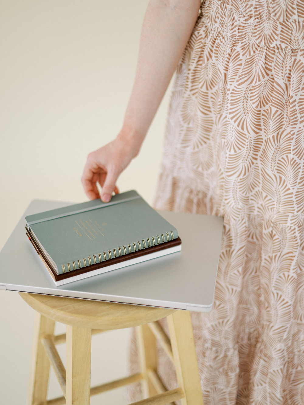 A soft, airy scene with notebooks stacked on a laptop as someone reaches to pick them up. A calm workspace moment perfect for planning Showit SEO updates.