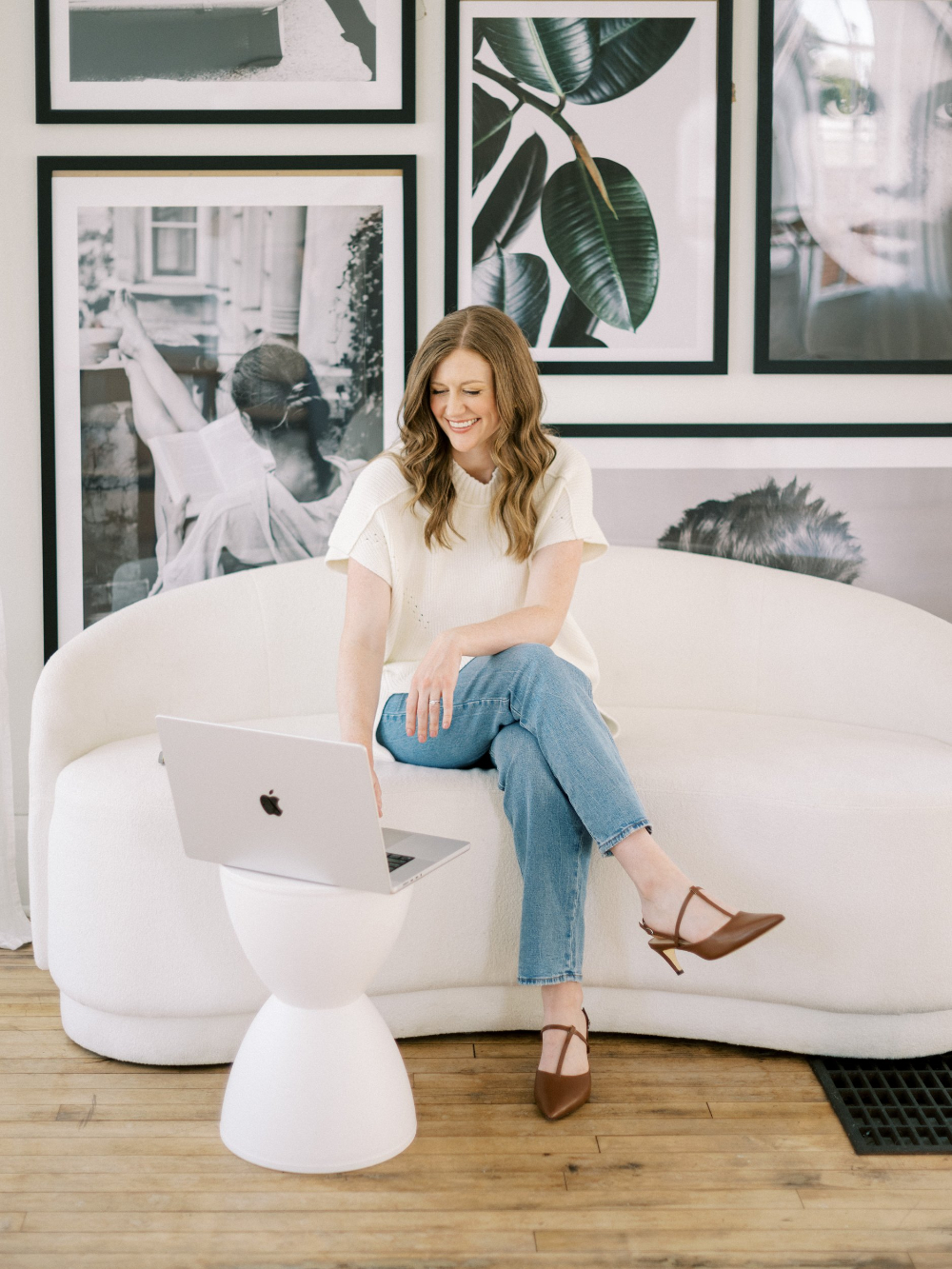 A woman sits on a white sofa with her laptop, smiling during work. A relaxed setting that reflects the ease of managing Showit SEO on a clean, modern site.