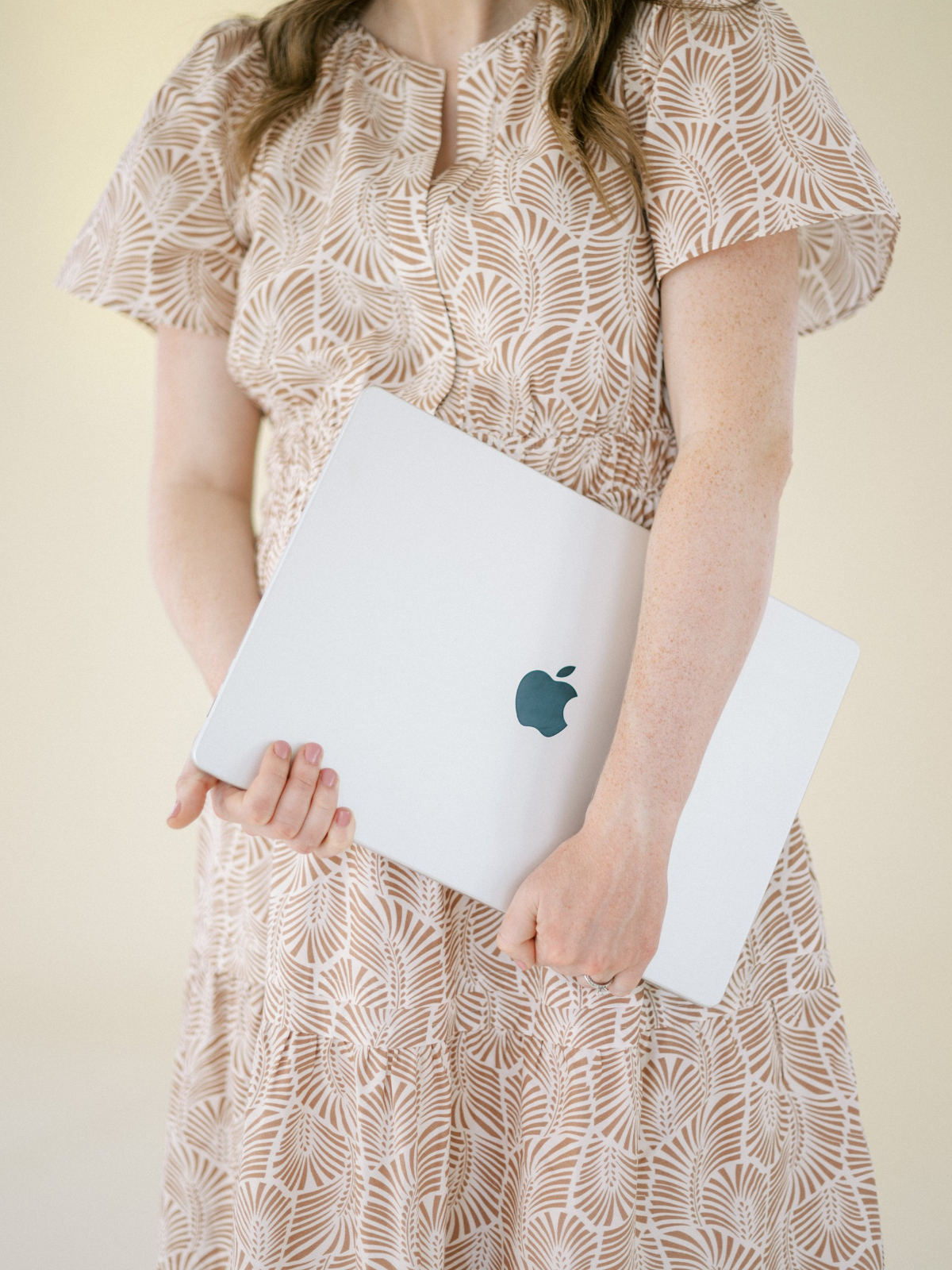 Close-up of a person holding a closed silver laptop against a patterned dress in a softly lit interior. | template vs custom website