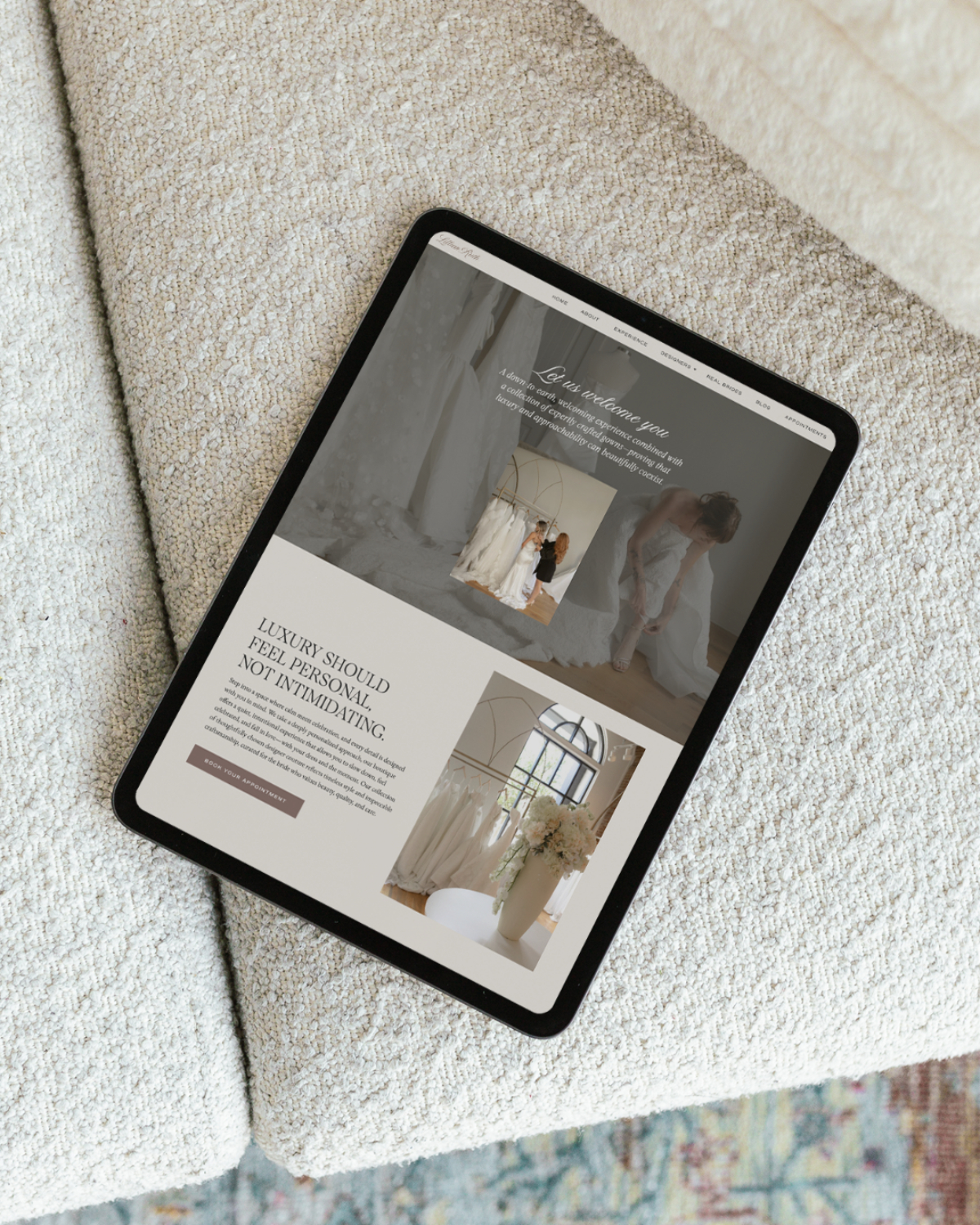 Tablet displaying a refined bridal shop website design placed on a textured sofa, showcasing imagery and copy.