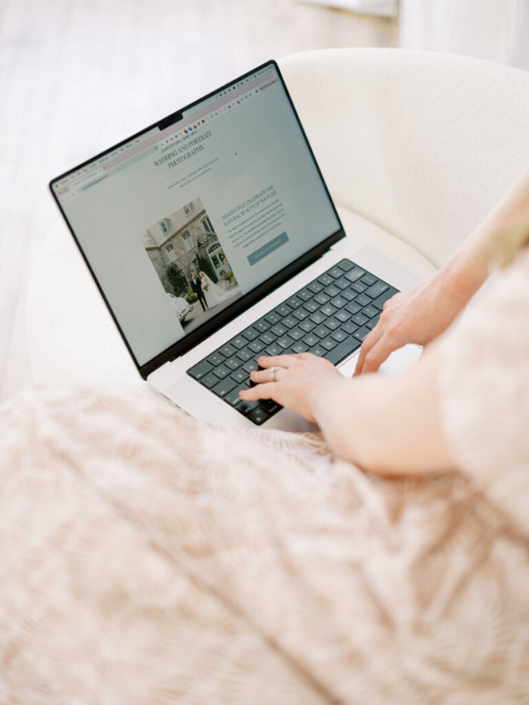 Person making website updates on Showit laptop, refining clean, high-end wedding website design at home