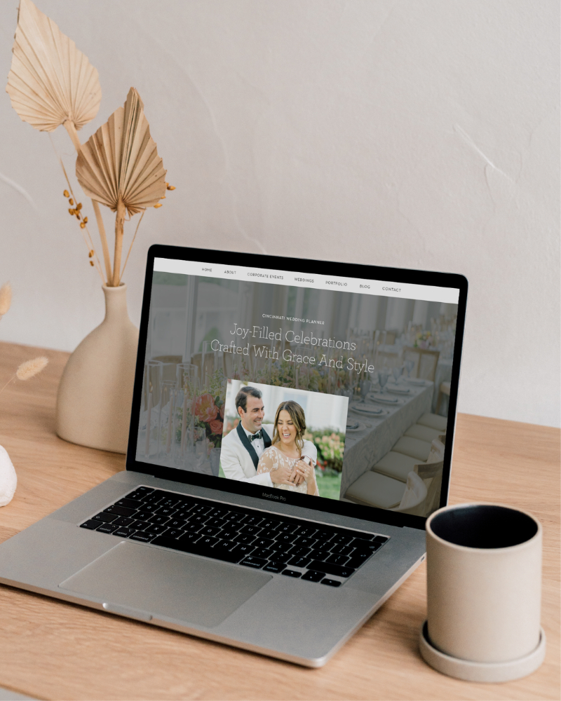 Laptop displaying a wedding website homepage on a clean desk beside a coffee mug